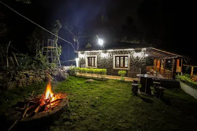 A campfire burning on the lawn in front of the lit Stone Villa at night