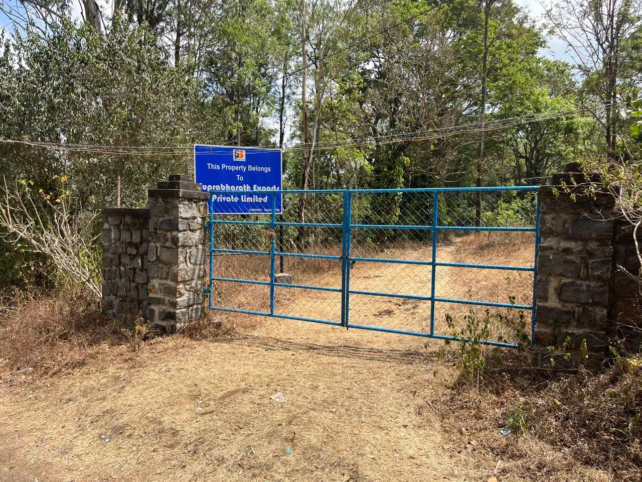 A blue gate between stone pillars, with a sign reading “This Property Belongs to Suprabharath Exports Private Limited”