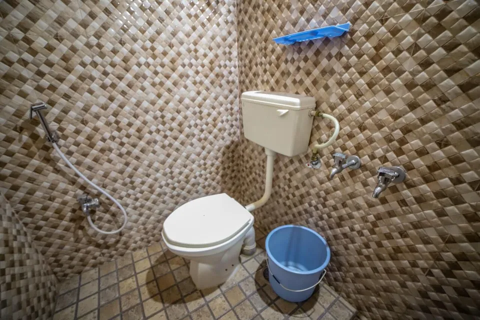 A bathroom with diamond-patterned tiles, a hand shower and a bucket