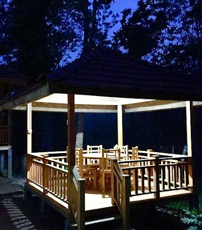The wooden gazebo glowing at dusk, its tables and chairs lit beneath the roof