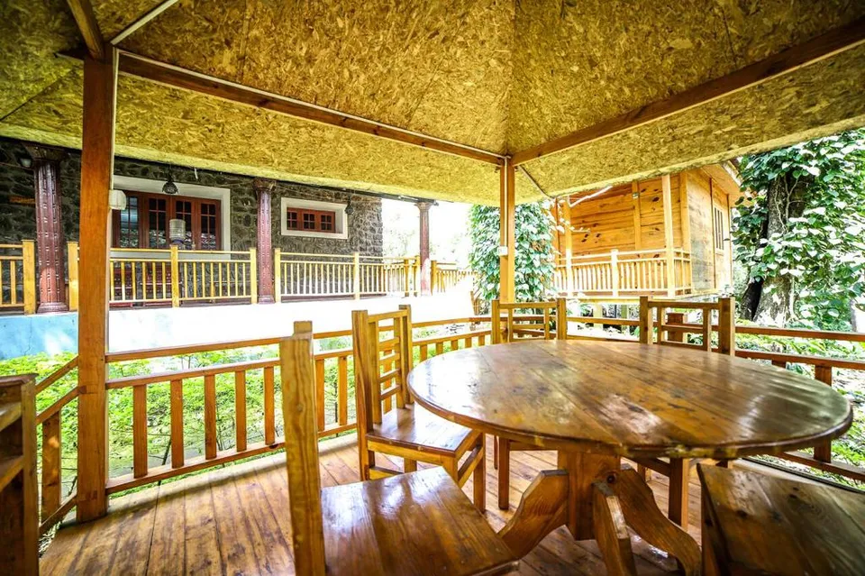 A round wooden table in the dining gazebo, with the Stone Villa and the Wooden Cottage behind it among pepper vines