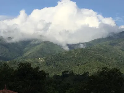 Towering white cloud over forested hills