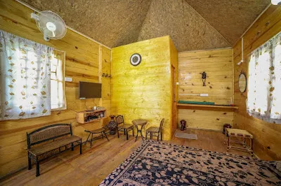 Inside the Wooden Cottage: timber walls, a bench, a small table with chairs and a patterned rug